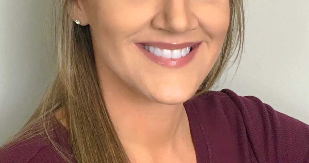 Headshot of a smiling woman with blond hair wearing a maroon top.