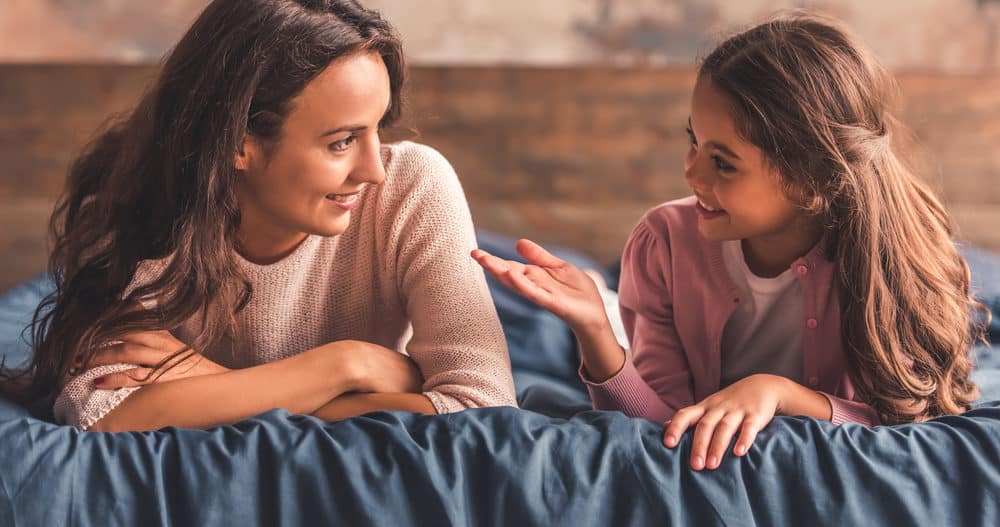 A mom and daughter talk about mental health while lying on a bed.