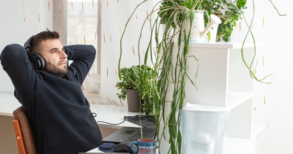 Man in office quiet quitting in the workplace and wearing headphones in relaxed position