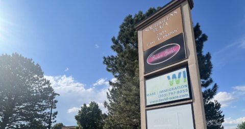 An outdoor shopping center sign against a backdrop of trees and blue sky