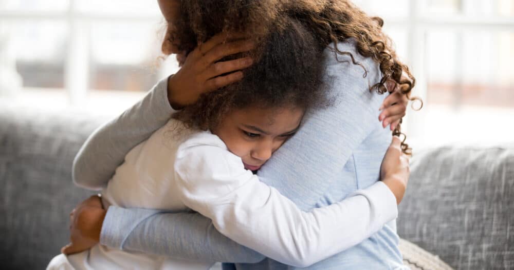 A mother embracing her young daughter while sitting on a blue and white couch