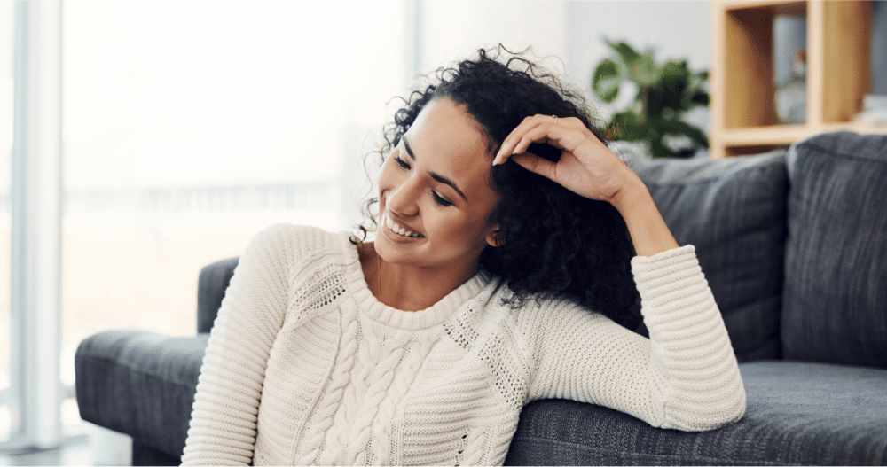 Woman leaning against the front of a couch smiling