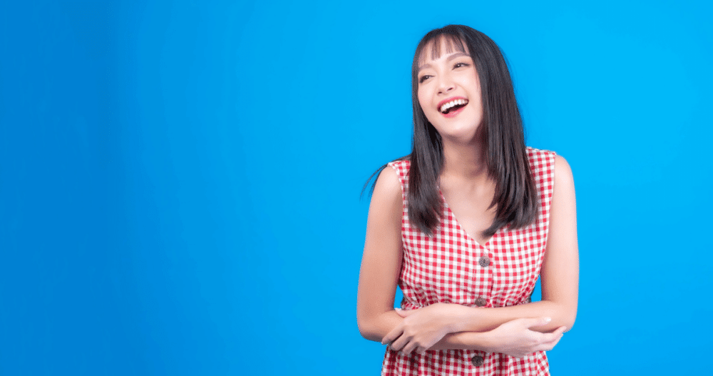 A smiling woman with long dark hair wearing a red and white checkered dress standing against a blue background