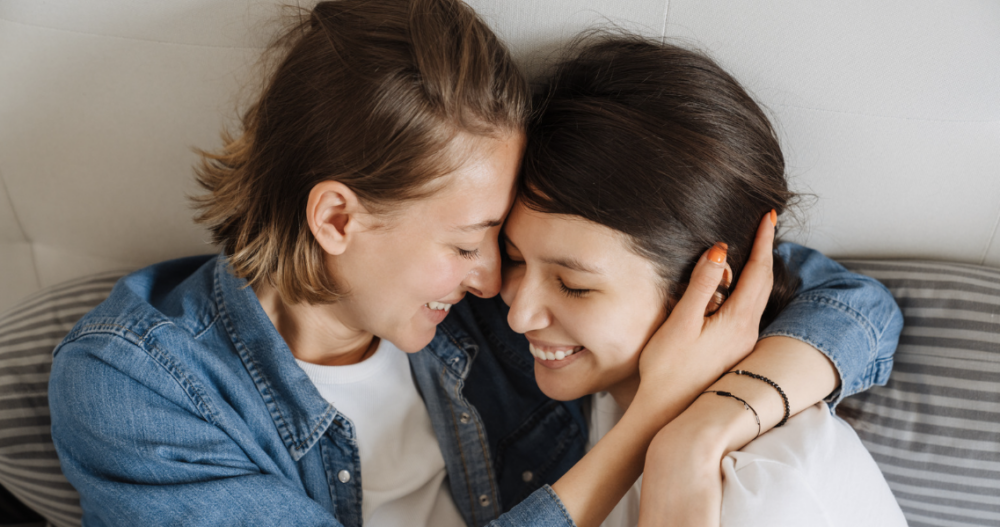 Two women in a relationship sitting on a couch embracing and smiling