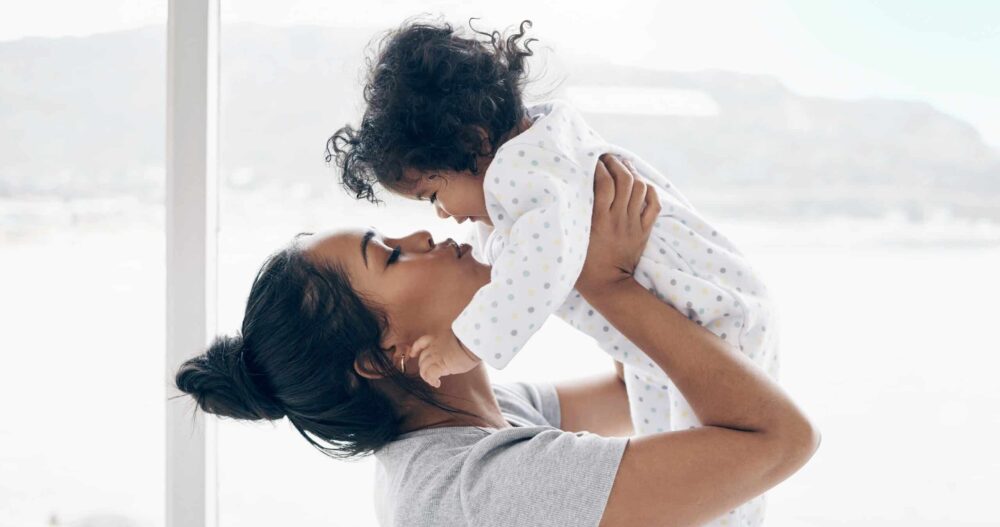 Mom holding her young child above her head and giving her a kiss