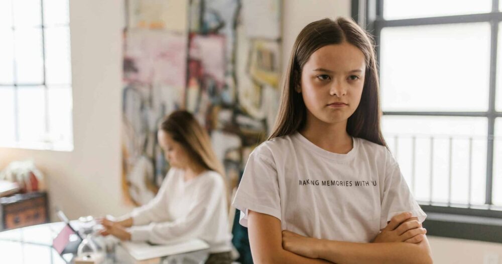 Girl facing away from her mom with her arms crossed and an angry look on her face