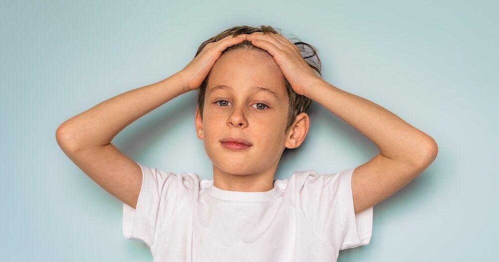 Portrait of a boy in a white t-shirt. The child folded his hands on his head and looks directly into the camera