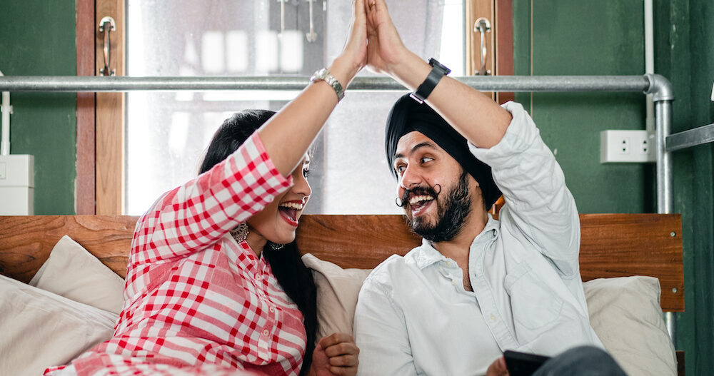 A couple sitting on a couch high fiving each other