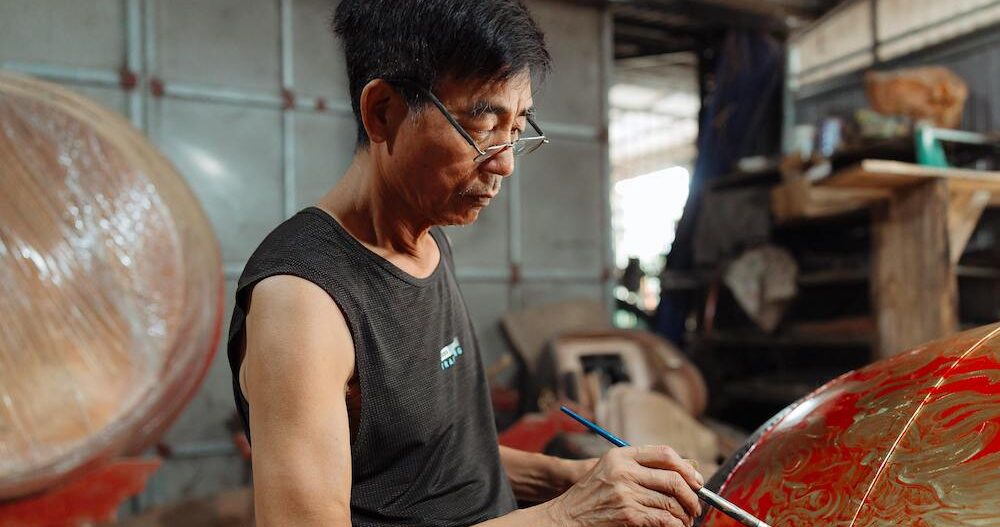Man in a workshop painting a dragon on a drum