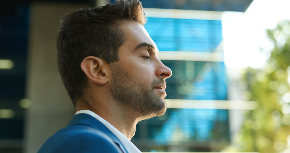Young businessman standing with his eyes closed and taking a deep breath outside during a break from work