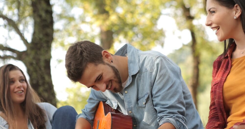 Man playing the guitar with some friends outside camping