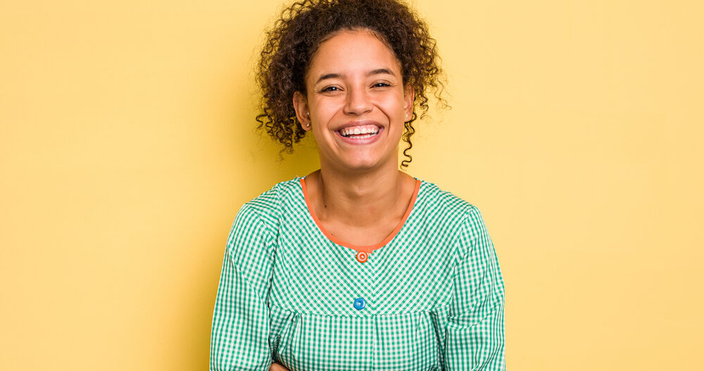 Teacher standing in front of a yellow wall laughing