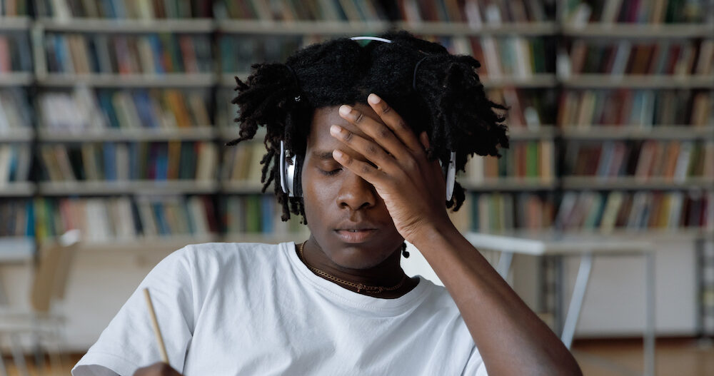 Student feels tired due to long preparations for college exam, deadline task, suffers from headache sit at table with laptop in library.