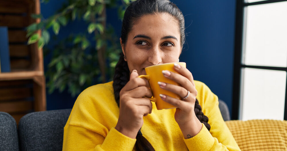 Young woman drinking coffee sitting on sofa at home