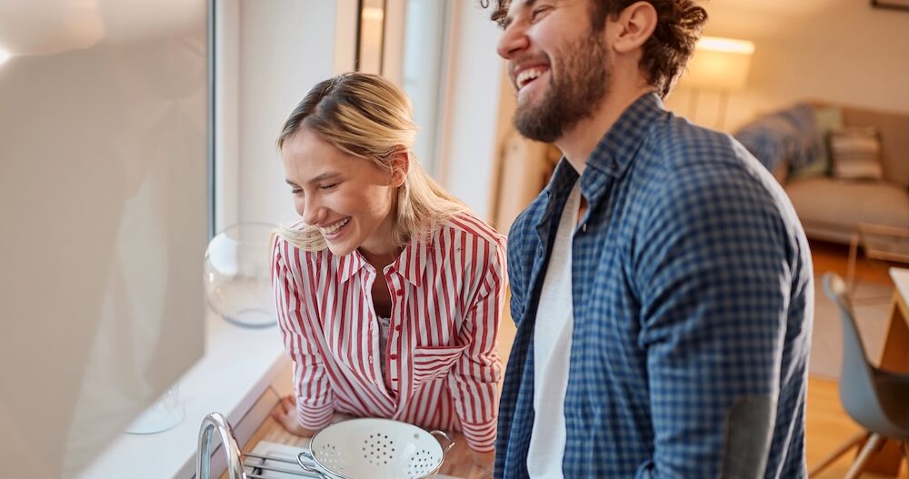 Man and woman laughing with each other while doing dishes