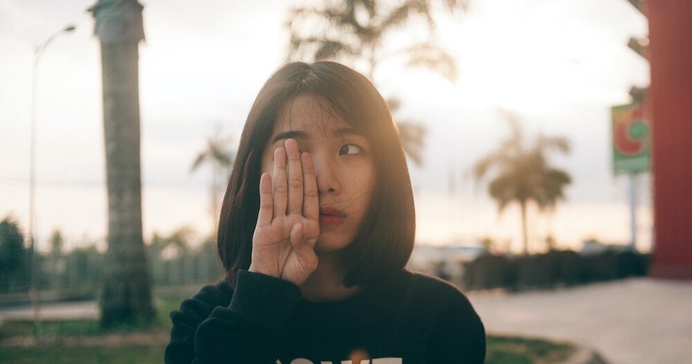 Woman standing outside covering one of her eyes with her hand