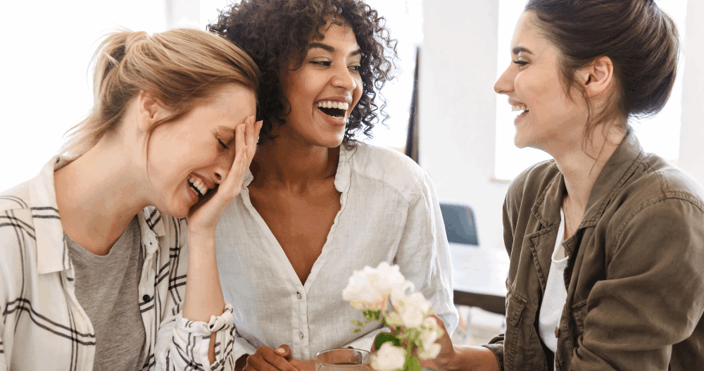 Three women sitting at a table in a coffee shop laughing together.